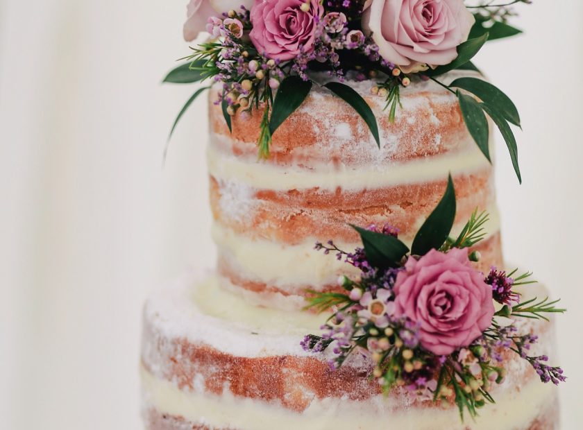 Close up of a three tiered, naked style wedding cake, with flower decorations